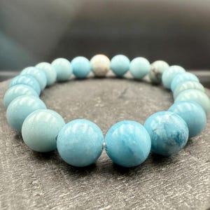 Puede incluir: Una pulsera el&aacute;stica compuesta por cuentas redondas y lisas de color azul claro. Las cuentas presentan variaciones de color, desde azul p&aacute;lido s&oacute;lido hasta patrones veteados con inclusiones blancas y azul oscuro, dispuestas en c&iacute;rculo.