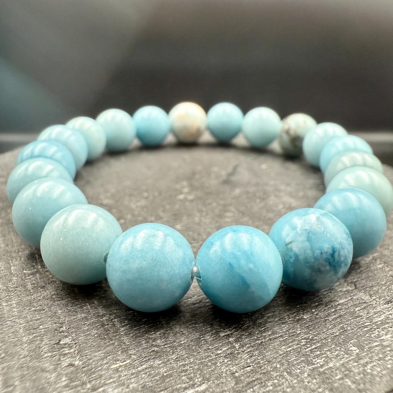 Puede incluir: Una pulsera el&aacute;stica compuesta por cuentas redondas y lisas de color azul claro. Las cuentas presentan variaciones de color, desde azul p&aacute;lido s&oacute;lido hasta patrones veteados con inclusiones blancas y azul oscuro, dispuestas en c&iacute;rculo.