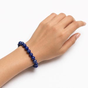 May include: A stretch bracelet composed of round, deep blue lapis lazuli beads. The beads feature subtle natural variations in color and texture, strung together in a continuous circular pattern to fit comfortably around the wrist.