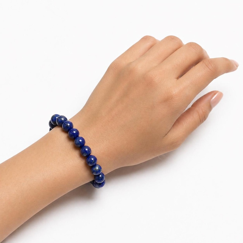 May include: A stretch bracelet composed of round, deep blue lapis lazuli beads. The beads feature subtle natural variations in color and texture, strung together in a continuous circular pattern to fit comfortably around the wrist.
