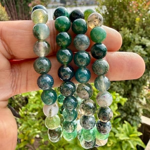 May include: Three strands of polished moss agate beads featuring a variety of green, white, and translucent tones. Each bead displays unique natural inclusions and patterns, ranging from deep forest green to pale mint and cloudy white hues.