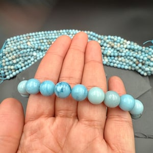 Puede incluir: Un hilo de cuentas redondas y pulidas de color azul claro con patrones de veteado natural en blanco y azul oscuro. Las cuentas son lisas y esf&eacute;ricas, y presentan un acabado brillante y uniforme en toda la longitud del hilo de cuentas.
