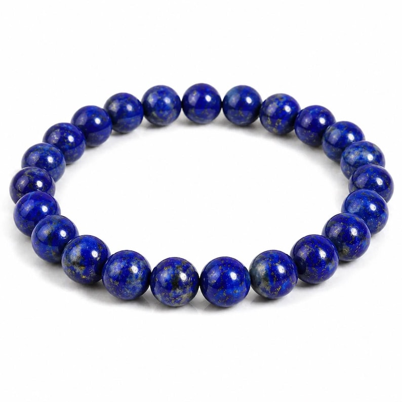 May include: A circular stretch bracelet composed of smooth, round, deep blue lapis lazuli beads. Each bead features natural variations in color, including subtle flecks of gold pyrite and darker blue inclusions, arranged in a continuous loop.