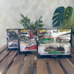May include: Several Hot Wheels Car Culture Team Transport sets. Each set includes a die-cast car and a matching truck or trailer. The cars feature various racing liveries, including Castrol and other designs. The packaging is black with the Hot Wheels logo.