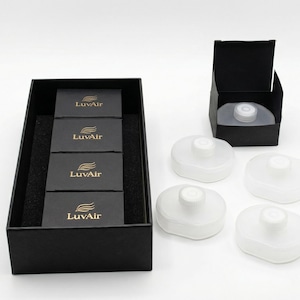 May include: A black box containing four smaller black boxes with the gold text "LuvAir". Beside the box are four white, rounded objects with a central raised portion. Another black box with a white object inside is also present.
