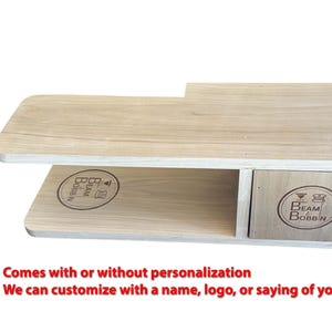 May include: A light-colored wooden sewing machine table with a drawer. The table has the words "BEAM BOBBIN" and a logo printed on it. The table is designed for sewing enthusiasts.