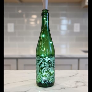 May include: A green glass bottle with a dragon design and string lights. The bottle has a light-colored stopper and is illuminated with small green lights. The dragon design is etched on the bottle.