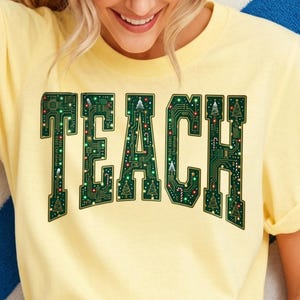 May include: A pale yellow short-sleeved t-shirt featuring the word TEACH in large block letters. The letters have a dark green circuit board pattern with small Christmas tree icons, candy canes, and tiny colorful lights integrated throughout.