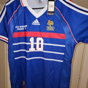 May include: A blue football shirt with white and red detailing. The shirt displays the number 10 in white, the Adidas logo, and text reading "FIFA WORLD CUP FRANCE 98". A tag is attached to the collar.