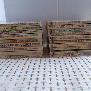 May include: A collection of vintage paperback books by Edgar Rice Burroughs, featuring titles like "The Land That Time Forgot" and "Escape on Venus." The books have off-white covers with titles in bold text.