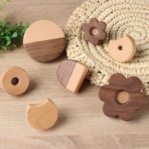 Pode incluir: Uma coleção de brinquedos de madeira em várias formas, incluindo um círculo, uma flor e um semicírculo. Os brinquedos são feitos de madeira castanha clara e escura. Alguns têm buracos no centro. Os brinquedos estão dispostos sobre uma esteira tecida.