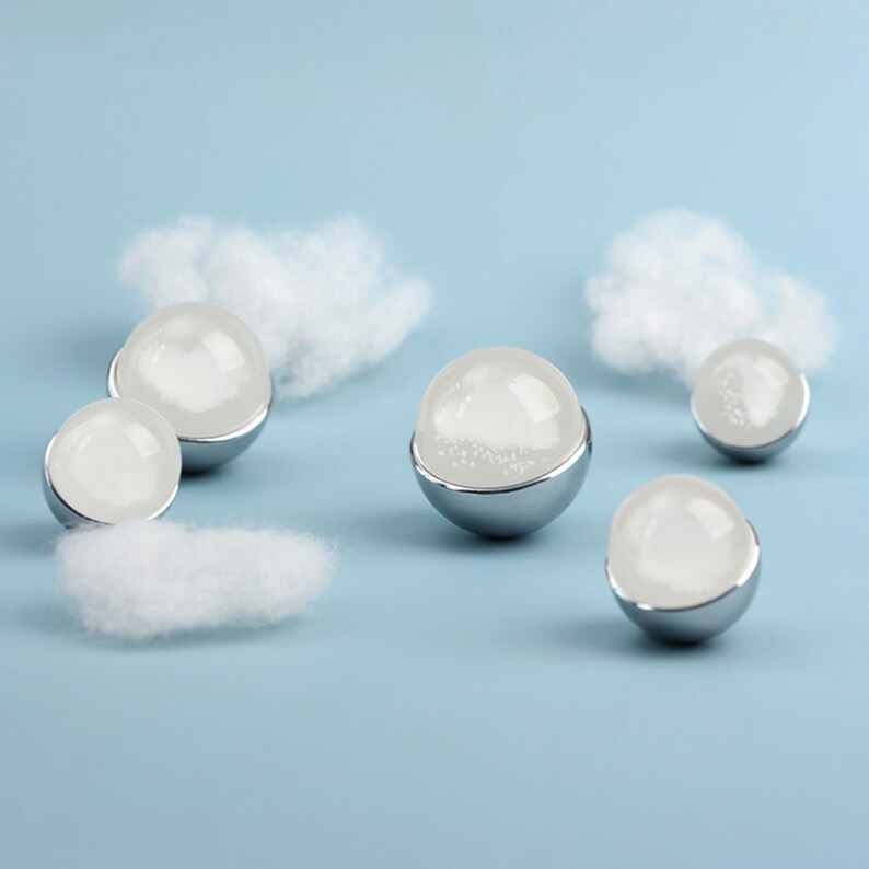 May include: A collection of six spherical objects with a clear, frosted appearance, each set in a silver-colored base. Fluffy white cloud-like shapes are scattered around the spheres against a light blue background. The objects appear to be decorative.