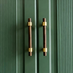 May include: Close-up of a green cabinet door with two dark brown wooden handles. Each handle is accented with a gold-colored band at the top and bottom. The cabinet door has vertical grooves.