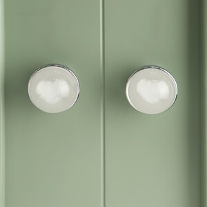 May include: A white ceramic mug with a black handle and the text "But First, Coffee" in a bold, black font. The mug is filled with a dark liquid, likely coffee, and sits on a light-colored surface.