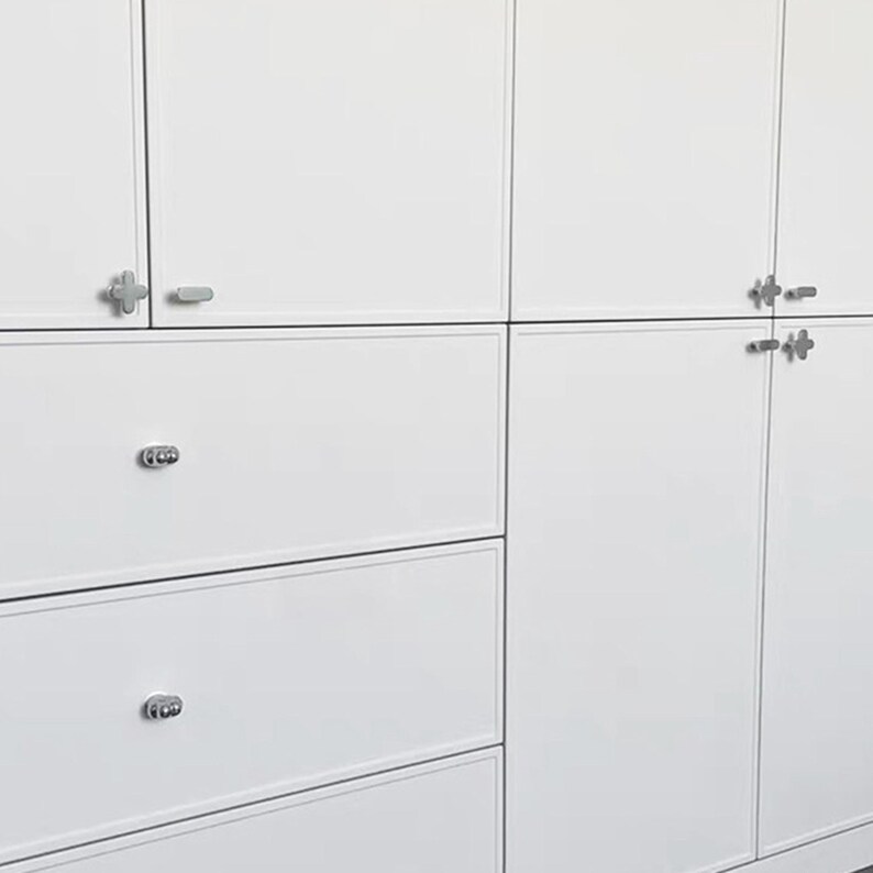 May include: White cabinets and drawers with silver-colored hardware. The cabinets have a clean, modern design with a smooth, glossy finish. The drawers have round, decorative pulls.