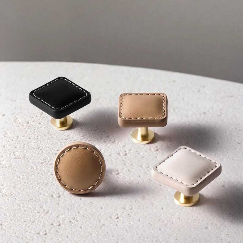 Może przedstawiać: Cztery dekoracyjne gałki do szafek o r&oacute;żnych kształtach: czarny romb, beżowy prostokąt, beżowe koło i biały romb. Każda gałka ma szytą obw&oacute;dkę i podstawę w kolorze złotym. Gałki te idealnie nadają się do dodania odrobiny elegancji meblom.