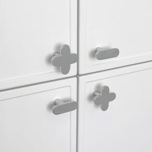 May include: Close-up of a white cabinet with four gray cabinet pulls. Two pulls are cross-shaped, and two are oval-shaped. The cabinet doors are white and have a simple, modern design.