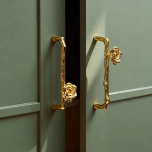 May include: Gold-colored cabinet pulls with a floral design. The pulls are shaped like branches with a flower at the end. The cabinet doors are a muted green color.