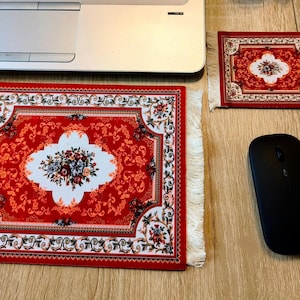 May include: A rectangular mouse mat and a smaller matching coaster, both featuring a red, white, and black floral pattern with white fringe on the ends. The mouse mat is positioned below a laptop, and a black computer mouse sits next to the coaster.