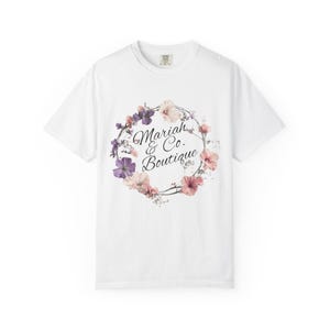 May include: White t-shirt with a floral wreath design and the text "Mariah & Co. Boutique". The wreath features pink, purple, and white flowers. The shirt has a crew neck.