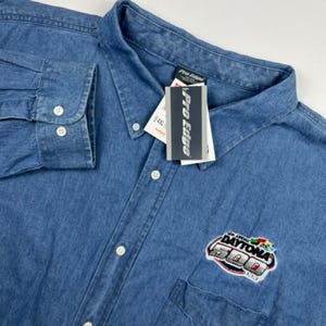 May include: A blue denim long-sleeve button-down shirt featuring a collar, a chest pocket, and a white tag with the text Pro Edge. An embroidered patch on the chest displays the text 42nd Annual Daytona 500 with a colorful race car graphic.