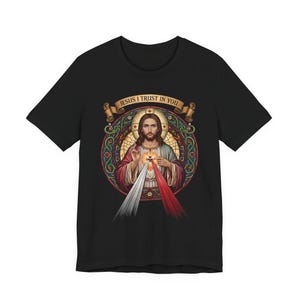 K&ouml;nnte beinhalten: Schwarzes T-Shirt mit religi&ouml;sem Motiv. Die Grafik zeigt eine Figur mit Heiligenschein, eingebettet in ein farbenfrohes Design im Glasmalerei-Stil. Der Text "JESUS I TRUST IN YOU" ist &uuml;ber der Figur zu sehen.