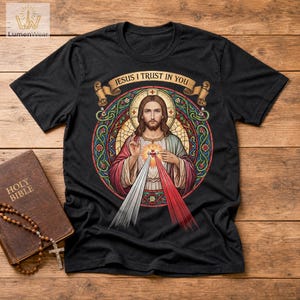 K&ouml;nnte beinhalten: Schwarzes T-Shirt mit einem Buntglas-Bild von Jesus und dem Text "JESUS I TRUST IN YOU". Eine braune Heilige Bibel und Rosenkranzperlen sind im Bild zu sehen.