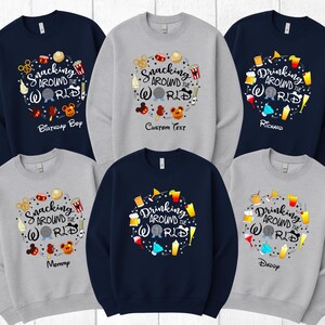 May include: Several navy and grey sweatshirts with vibrant graphic designs. The designs feature the phrases "Snacking Around the World" and "Drinking Around the World", accompanied by food and drink illustrations. Some sweatshirts have custom text.