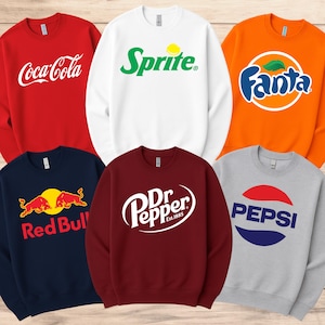 Könnte beinhalten: Eine Auswahl an Sweatshirts mit Rundhalsausschnitt in verschiedenen Farben, die jeweils das Logo einer beliebten Getränkemarke zeigen. Die Sweatshirts umfassen Coca-Cola in Rot, Sprite in Weiß, Fanta in Orange, Red Bull in Marineblau, Dr. Pepper in Burgunderrot und Pepsi in Grau.