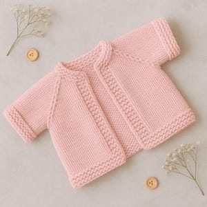 Può includere: Un cardigan per neonati lavorato a maglia rosa chiaro. Il maglione aperto sul davanti presenta colletto, polsini e orlo a coste. Le cuciture decorative corrono lungo i bordi anteriori. Le maniche sono inserite. Un bottone di legno e rametti di fiori bianchi sono sullo sfondo.