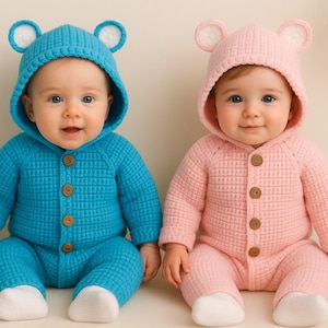 May include: Two babies wearing matching bear-eared hooded jumpsuits. One is turquoise blue, the other is light pink. Both outfits have wooden buttons and white foot coverings. The babies are sitting and smiling.