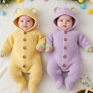 Puede incluir: Dos bebés con monos con capucha de ganchillo hechos a mano. Uno es amarillo con ribetes verdes, el otro es lavanda con ribetes verdes. Ambos tienen botones de madera y orejas de oso en la capucha. Decoraciones de Pascua en el fondo.