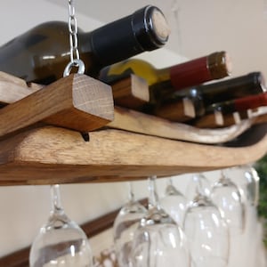May include: A wooden wine rack with a curved design, hanging from the ceiling. The rack holds multiple wine bottles and has a separate section for hanging wine glasses.