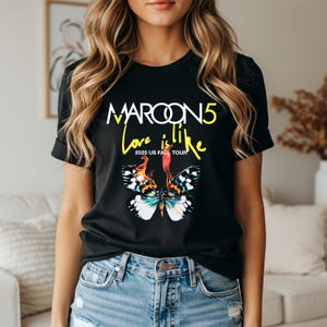 May include: Black t-shirt featuring the text "MAROON 5 Love is like" in yellow and white, with a butterfly graphic. The shirt also includes "2025 US FALL TOUR" in yellow text.