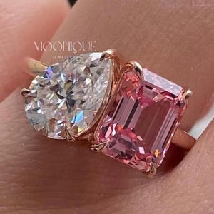 May include: Elegant Toi Et Moi engagement ring featuring a sparkling pear cut moissanite paired with a vibrant emerald cut pink sapphire in a modern two stone design. Handcrafted in solid 14K gold with a sleek polished band, this unique bridal ring symbolizes two souls united in timeless love. The text "BY MOONIQUEJEWELLERY" is visible at the bottom.