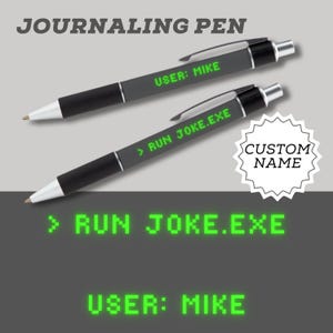 Peut inclure: Deux stylos de journalisation noirs et gris avec des détails argentés. L'un des stylos affiche "USER: MIKE" en vert, l'autre affiche "> RUN JOKE.EXE". L'image affiche également le texte "CUSTOM NAME", "> RUN JOKE.EXE" et "USER: MIKE" en vert.