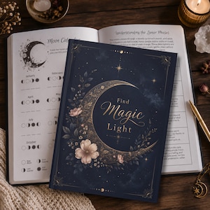 Op de afbeelding: Een donkerblauw notitieboek met harde kaft en een gouden halve maan en bloemenillustratie op de omslag. De tekst luidt Find Magic Light. Het notitieboek ligt open en toont een maankalender en de tekst Understanding the Lunar Phases.