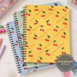 May include: Three spiral-bound notebooks with a cherry pattern and the text "Doing My Best" printed in a repeating script. The top notebook is yellow, the middle is light green, and the bottom is light blue. Each notebook measures 8.5 by 11 inches.