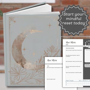 Op de afbeelding: Een lichtgrijs hardcover dagboek met een halve maan en bloemillustraties in roségoudfolie op de kaft. De tekst "Start your mindful reset today" staat in een donkergrijze ster. De binnenpagina's tonen "New Moon"-planningssjablonen.