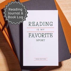 May include: A white reading journal and book log with dark green text that reads Reading Is My Favorite Sport and 2026 Edition, featuring red dotted lines. The journal is placed on top of a dark gray notebook and a tan notebook with a black pen.