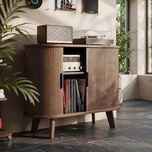 May include: A mid-century modern style wooden record cabinet with a speaker and turntable on top. The cabinet has a ribbed design and holds vinyl records. A wall-mounted record and album art are visible in the background.