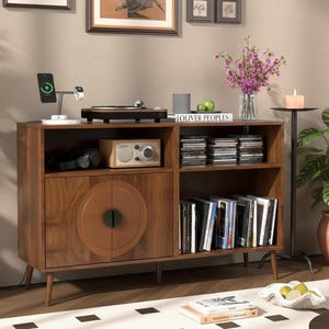 May include: A mid-century modern style wooden media console with a record player, radio, and storage for CDs and books. The console is brown with a circular design on the cabinet doors. A charging station and plants are also visible.