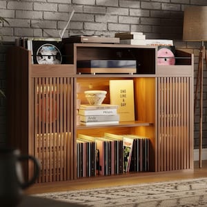 May include: A wooden media cabinet with vertical slat doors and open shelving. The cabinet holds vinyl records, books, and a record player. A lamp and a plant are visible in the background. The cabinet has a warm, inviting aesthetic.