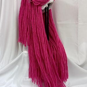 Può includere: Una parrucca rosa vibrante con ciocche lunghe e dritte. La parrucca presenta un cappuccio bianco ed è adornata da un fiocco rosa chiaro trasparente. La parrucca è progettata per essere indossata ed è probabilmente per costumi o cosplay.