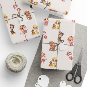 May include: Wrapped gifts with a light beige background, decorated with watercolour illustrations of cartoon puppies in different poses. The gifts are tied with twine and have small white tags. A ball of twine, scissors, and blank tags are also visible.