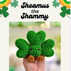 Pode incluir: Um brinquedo de pelúcia de trevo verde feito à mão com um rosto sorridente e pés castanhos. O texto "Sheamus the Shammy" está acima do brinquedo de pelúcia, com gráficos de trevos e arco-íris.
