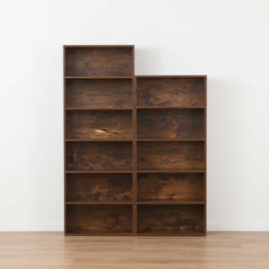 May include: Two dark brown wooden bookshelves with multiple shelves. The shelves are arranged in a stacked configuration, with one unit taller than the other. The wood grain is visible, and the shelves are empty.