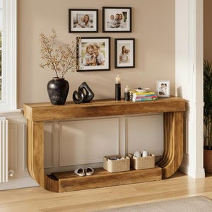 May include: A solid oak console table with a curved design, featuring a lower shelf and a display surface. The table is decorated with a black vase, abstract sculpture, candles, and framed photos. Two woven baskets and slippers are on the lower shelf.