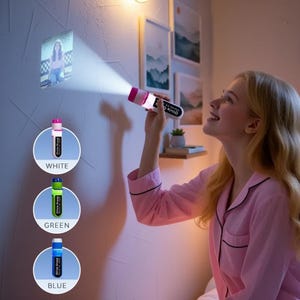 Puede incluir: Una mujer en pijama rosa sostiene una linterna blanca y rosa que proyecta una imagen en una pared. La linterna está etiquetada como "Olivia Grace". Se muestran tres marcadores etiquetados como "Blanco", "Verde" y "Azul".