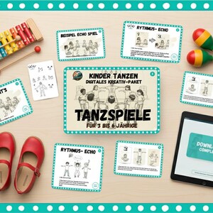 Puede incluir: Un xilófono colorido, maracas y zapatos rojos están dispuestos con tarjetas y una tableta sobre una superficie de madera. La tableta muestra "Download Complete". Las tarjetas presentan ilustraciones y texto en alemán, incluyendo "Kinder Tanzen".